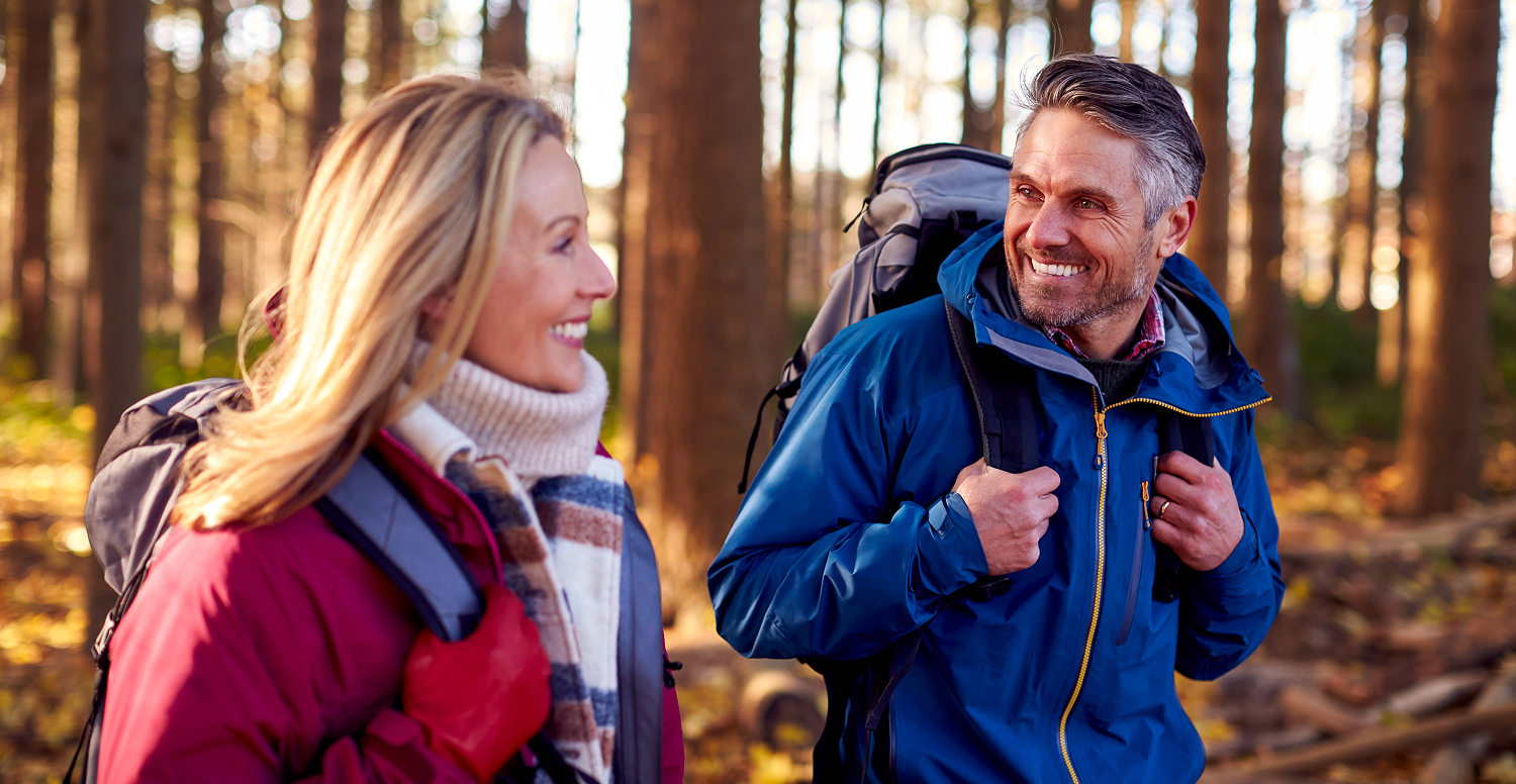 A middle-aged couple trekking through a pine forest.
